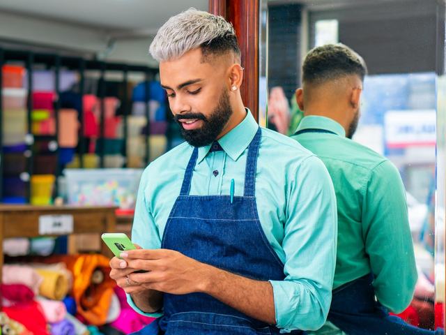 Vendedor de avental confere o celular no balcão de uma loja de tecidos